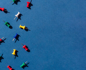 Colorful push pins or thumbtacks frame on the blue background. Top view. Copy space