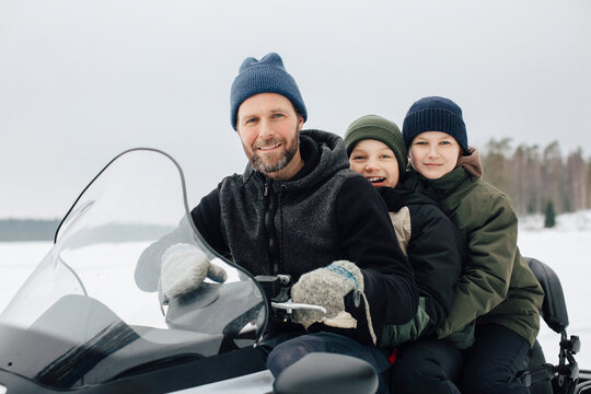 Portrait of smiling man traveling with boys on snowmobile during winter
