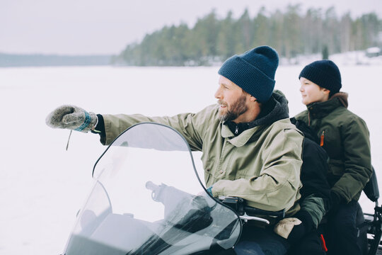 Mature man gesturing while snowmobiling with boys