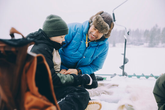 Happy father talking with son sitting on frozen lake - Powered by Adobe