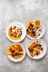 Overhead view of plate with breakfast crepes with berries and bananas on light surface