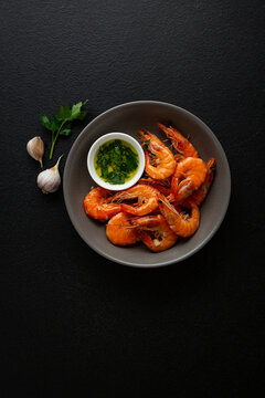 Top view of cooked prawn in shell seafood shrimps with green sauce on black background