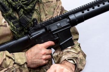 A military man in camouflage holds an American automatic rifle in his hands on a light background, close-up. Concept: military action, soldier of fortune.