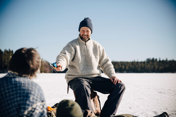 Smiling mature man giving fishing rod to friend during sunny day