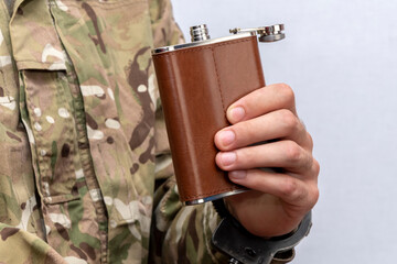A soldier in a military camouflage uniform is handcuffed, holding a flask in his hand on a light...