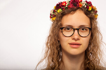 Portrait of a young girl in glasses on a white background. A girl with curly hair with a wreath on her head. Natural beauty and youth. Pleasant face of a light-skinned girl