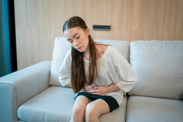 Young woman suffering from abdominal pain while resting on sofa at home