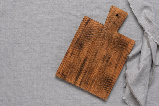 Empty wooden cutting board and linen napkin on gray textile background. Top view, flat lay.