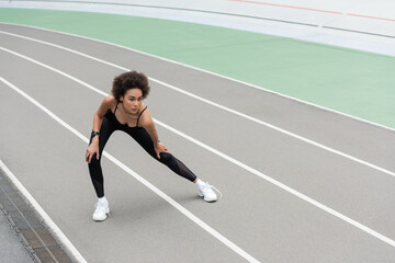 Fototapeta na wymiar young african american woman warming up on stadium while doing side lunge exercise.