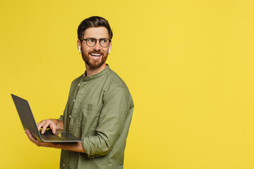 Remote job concept. Happy man with laptop in hands looking aside at copy space, standing on yellow background - obrazy, fototapety, plakaty