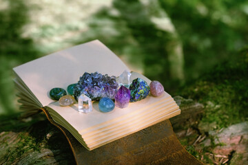 witch spell book and minerals on natural blurred forest background. Gemstones for healing Magic...
