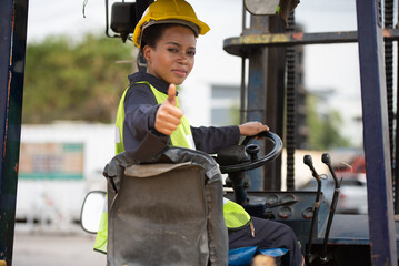 Female worker driving forklift in industrial container warehouse, raised thumbs up, good job. - 527360273