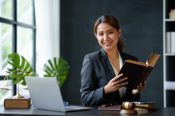 Beautiful Asian woman lawyer sitting at a table smiling happy with a laptop computer with law books hammer and scales hammer and scale.