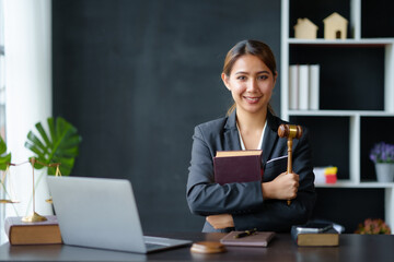 Beautiful Asian woman lawyer sitting at a table smiling happy with a laptop computer with law books...