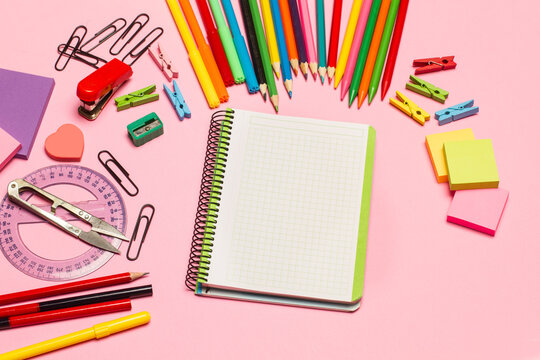 Cuaderno en blanco, boli, post it, bloc, clips, lapices y accesorios sobre un fondo rosa pastel liso. Vista superior y de cerca. Copy space