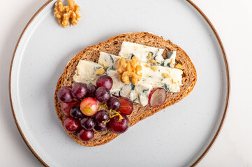Fototapeta na wymiar Toasted bread with mild creamy blue cheese, grapes and walnuts on grey plate