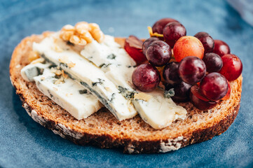 Toasted bread with mild creamy blue cheese, grapes and walnuts on grey plate