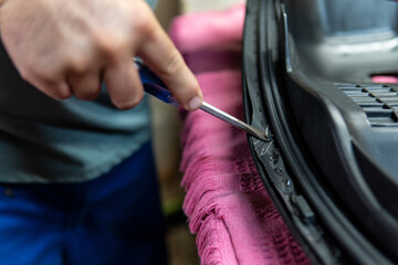 Close-up shot of an upholsterer's hands removing staples from a leather motorbike seat.