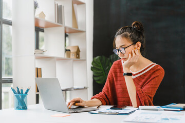 Bored asian nerd lady working with laptop computer when sitting at desk.