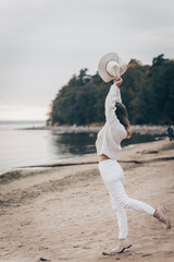 blonde girl in a white hat walks along the seashore on an autumn day