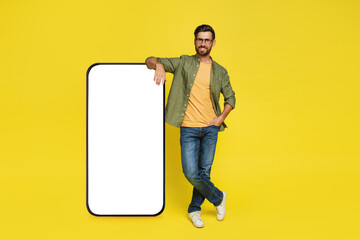 Full body length of man leaning on big smartphone with empty white screen, standing on yellow...