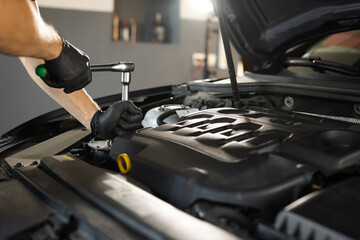 Close Up of Male Mechanic Working on a Car in a Car Service. Empowering Man Makes an Usual Car Maintenance. He's Using a Ratchet. Modern Clean Workshop. Auto Service