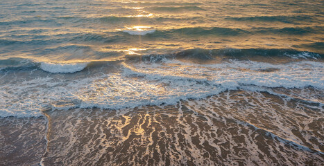 Calm ocean waves rolling onto sandy beach at sunrise