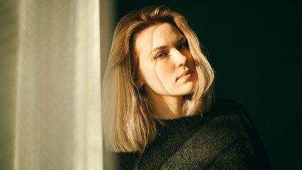 Blonde girl in a room near the window with a shadow on her face