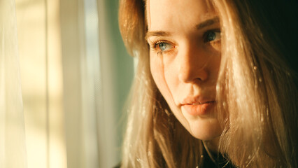 Blonde girl in a room near the window with a shadow on her face