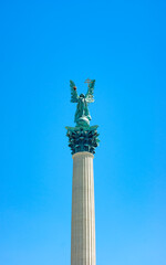 Fototapeta na wymiar Angel Gabriel statue in Heroes Square, Budapest, Hungary. The traditional guardian holds the crown of St Stephen and a two-barred apostolic cross, that recognizes converting Hungary to Christianity.