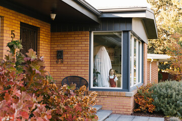 Little girl (2-3) and father dressed as Halloween ghost standing in window