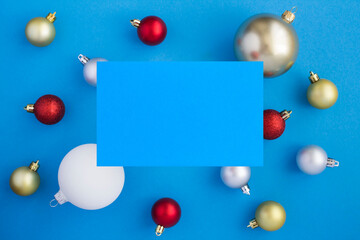 Christmas colored balls and greeting card for text on the blue background. Copy space. Top view.