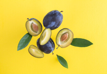 Flying in air fresh ripe whole and cut blue plums with leavs on the yellow background. Close-up.