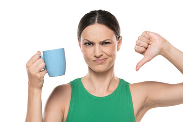 dissatisfied young woman with cup of hot beverage showing thumb down on a white background.