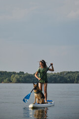 Stand up paddle with pet. Concept animals actively spend time with the owner. Young Caucasian woman...