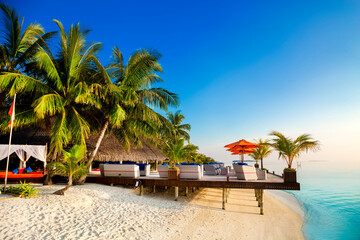 Naklejka premium Landscape on Maldives island, luxury water villas resort and wooden pier. Beautiful sky and ocean and beach with palms background for summer vacation holiday and travel concept. Luxury travel.