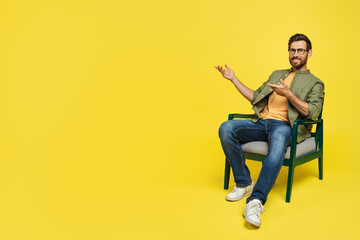 Happy middle aged man sitting on chair and showing free space aside, advertising offer, demonstrating your design