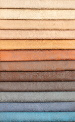 Fabric swatches in different colors are stacked for selection. A variety of shades of upholstery material for furniture and interior. Fabric texture close up. A set of multi-colored rolls of material.