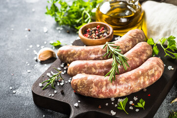 Bratwurst or sausages on cutting board with spices at black table. Ready for cooking.