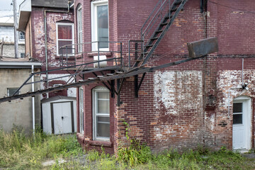 Fototapeta na wymiar Exterior of abandoned run down two storey red brick house with large steel fire escape in a weedy lot, daytime, nobody