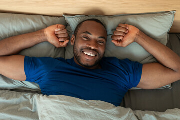 Happy Black Man Awakening After Sleep Stretching Lying In Bedroom