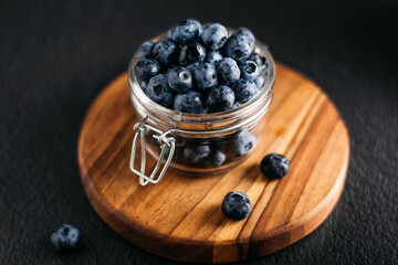 
a jar of blueberries on a wooden board, dark background