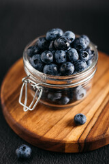 
a jar of blueberries on a wooden board, dark background