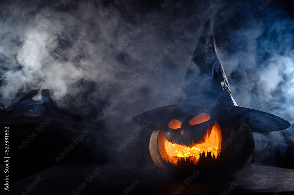 Wall mural a creepy pumpkin with a carved grimace in the smoke. jack o lantern in the dark.