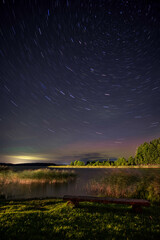 Beautiful star filled sky with star trails above a calm lake with a bench
