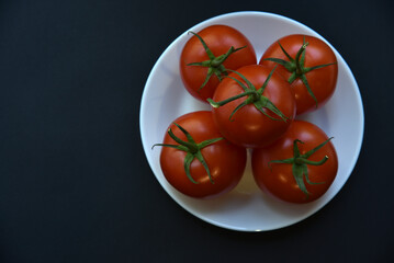 Red juicy tomatoes on a white plate. Delicious tomatoes on a black background.