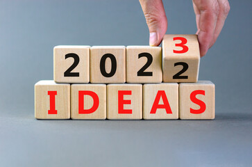 2023 ideas new year symbol. Businessman turns a wooden cube and changes words Ideas 2022 to Ideas 2023. Beautiful grey table grey background, copy space. Business 2023 ideas new year concept.