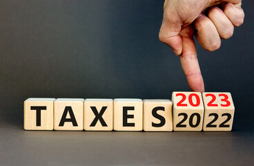 2023 taxes new year symbol. Businessman turns a wooden cube and changes words Taxes 2022 to Taxes...