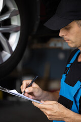 Car service employe inspect car. Mechanic inspects the car undercarriage way and makes a note on...