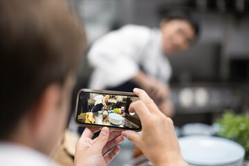 Chef photographing colleague preparing food in restaurant